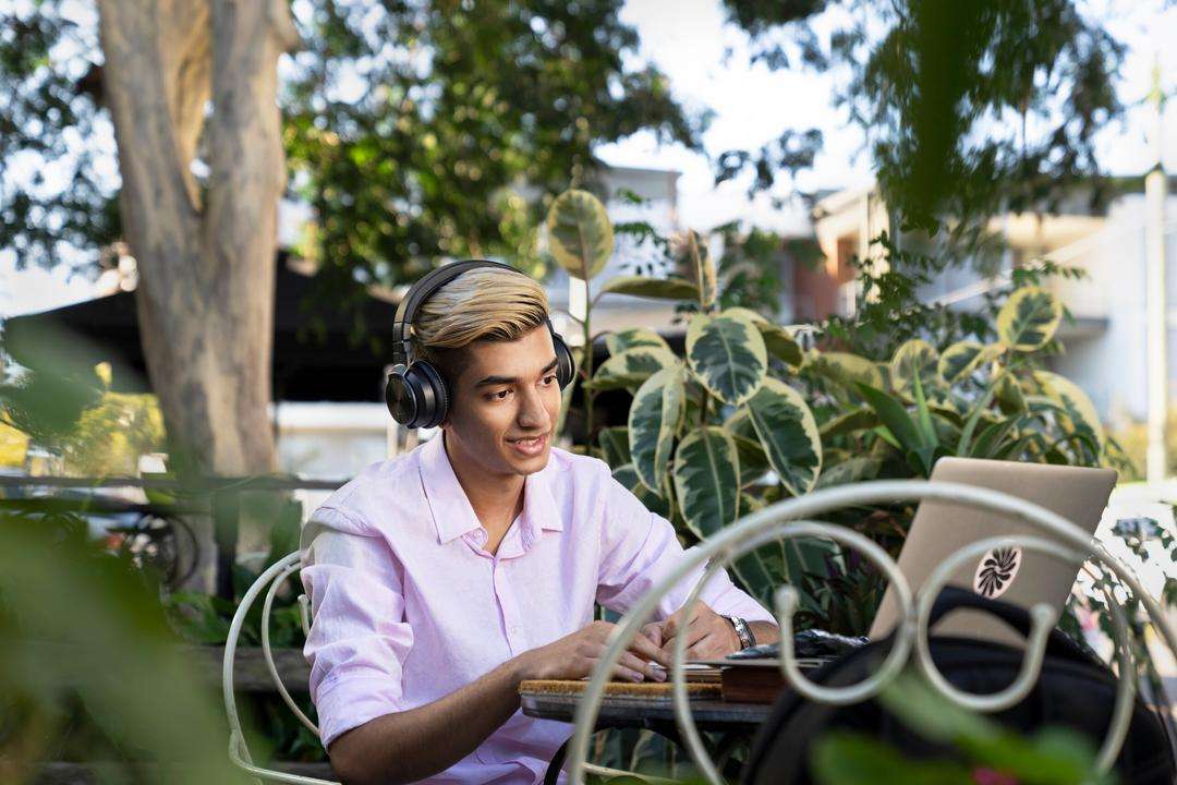 CQU student smiling and sitting outside at a bench and using his laptop