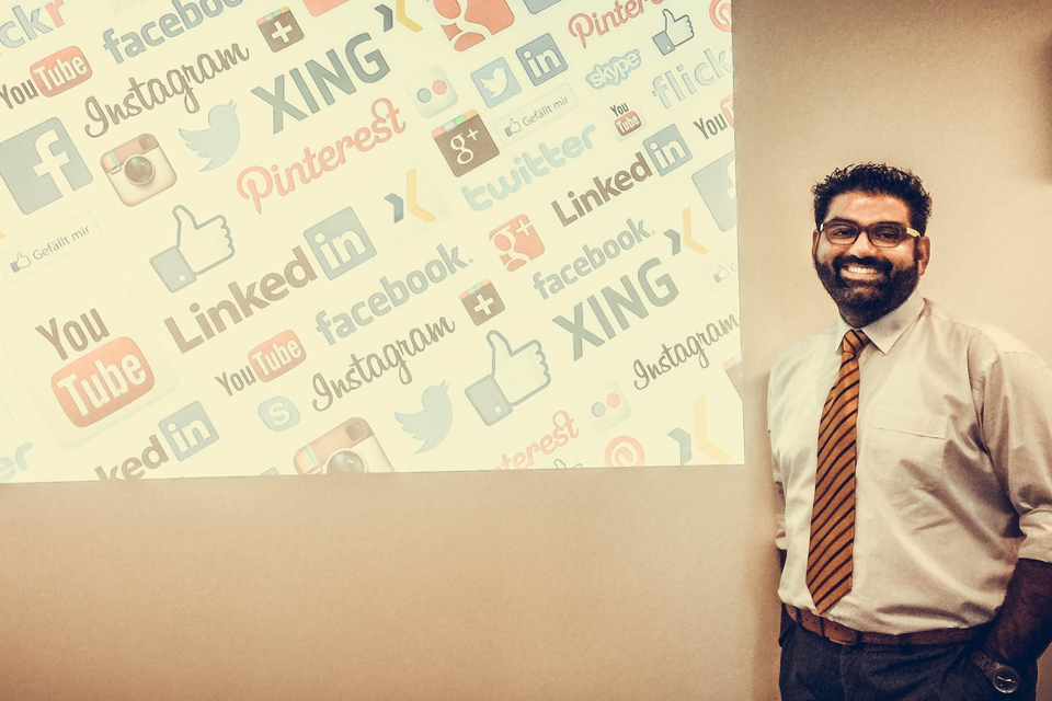 Ritesh smiling next to a projection of social media logos on a wall