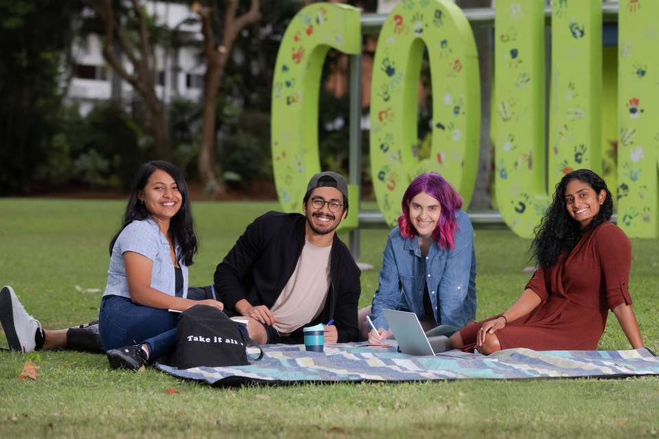 Smiling CQU male and female students sitting on grass at Rockhampton Campus.