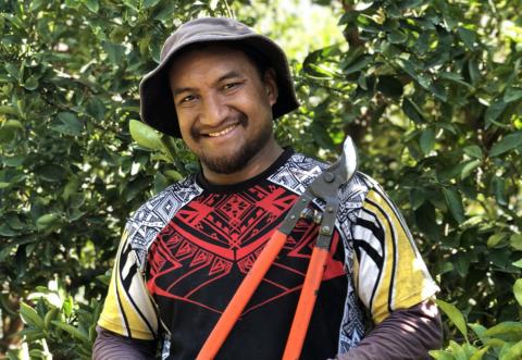 Anthon Wasang smiling at the camera as they hold secateurs and wear a hat in an orchard