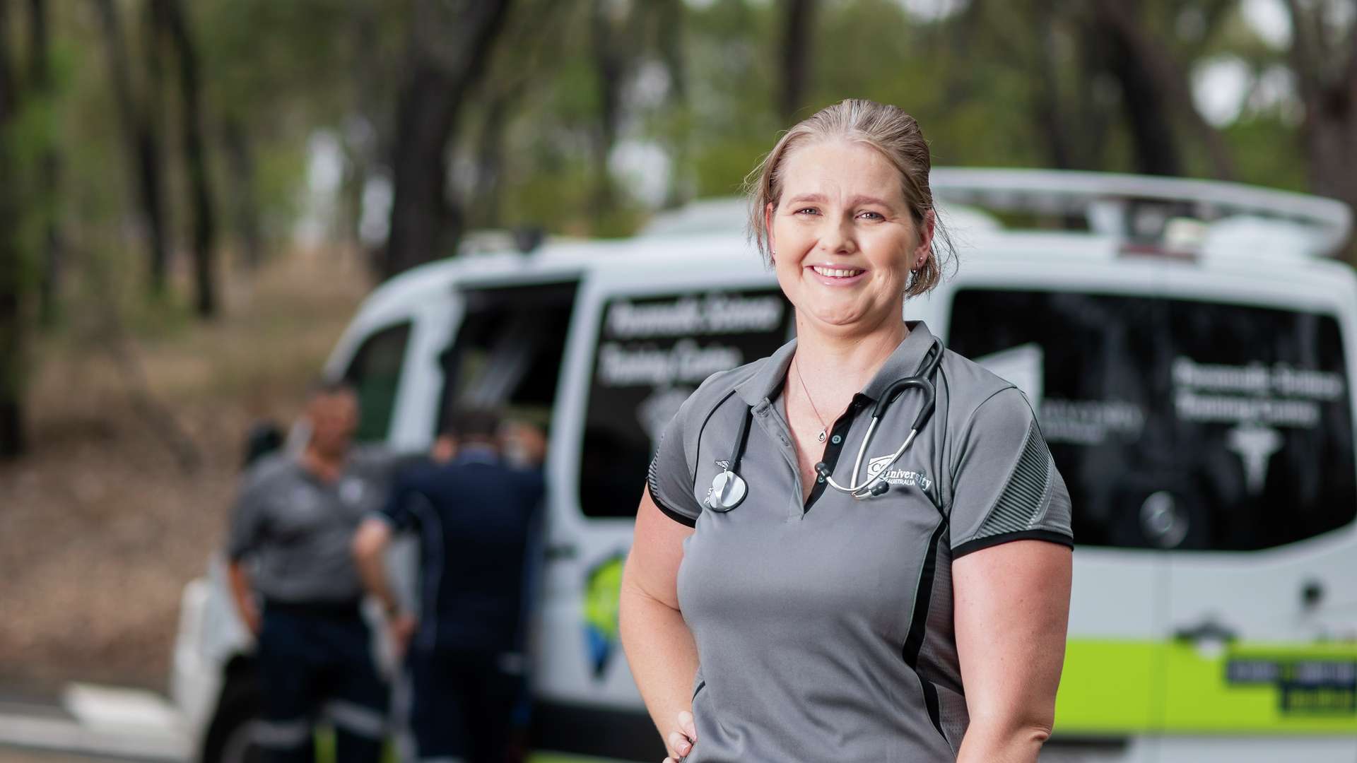 a student paramedic holding an emergency kit bag in front of an ambulance