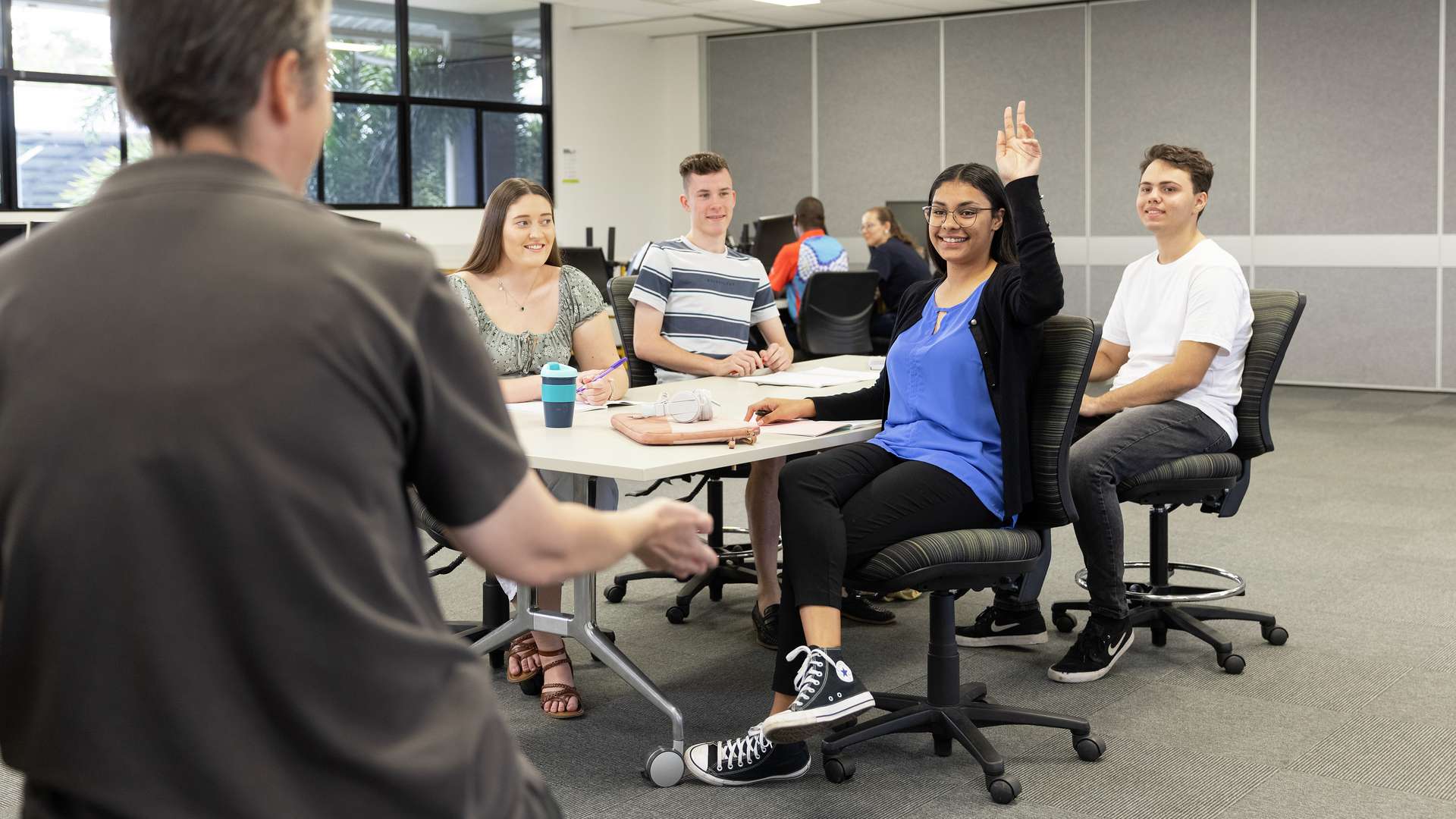 CQU student raises her hand to ask a question in a classroom with other students.