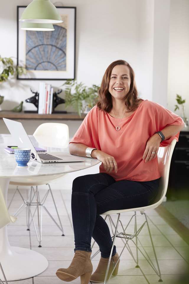 Person smiling at camera and sitting at white table with laptop studying.