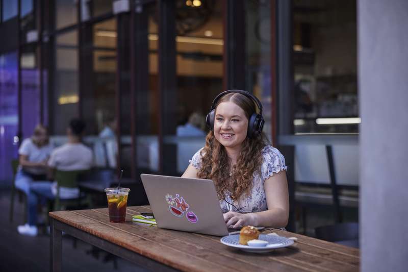 High School student sitting outside a cafe with a laptop and headphones studying