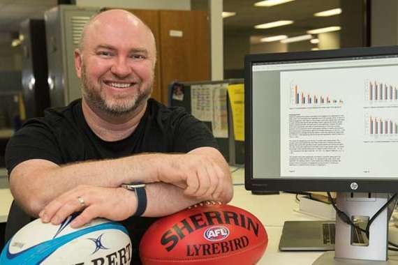 Dr Alex Russell holding two footballs in front of gambling statistics
