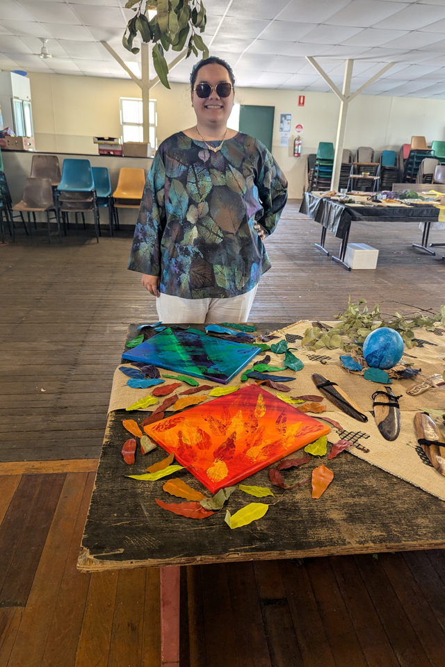 Jirrbal artist Annette Lenahan stands behind a table displaying colorful artworks.