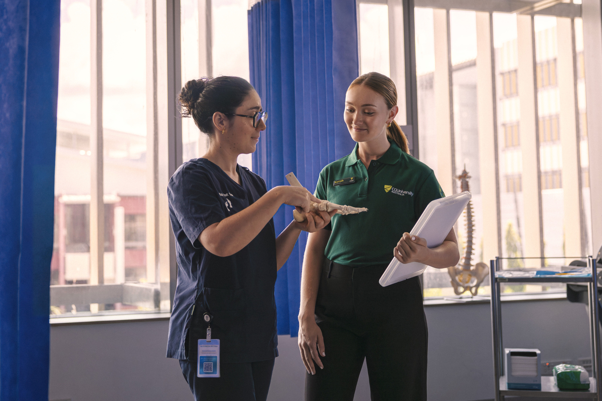 Student chatting with QLD health staff member as they hold a model of a foot in a hospital setting
