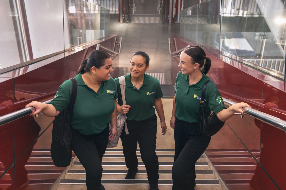 Three students in CQU shirts walking up stairs in a QLD health facility