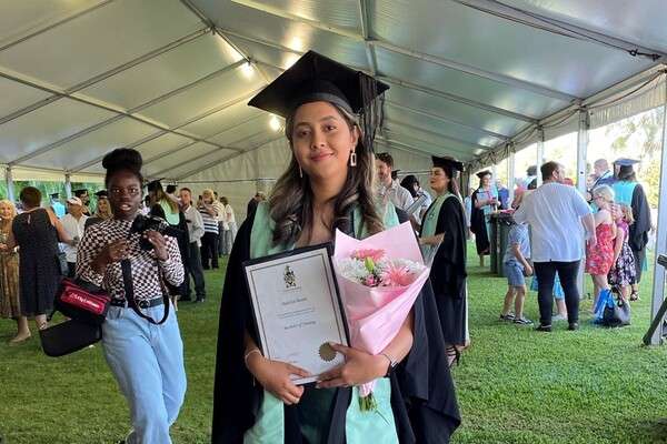 Rakshya Basnet in graduation regalia holding a bunch of flowers and their certificate