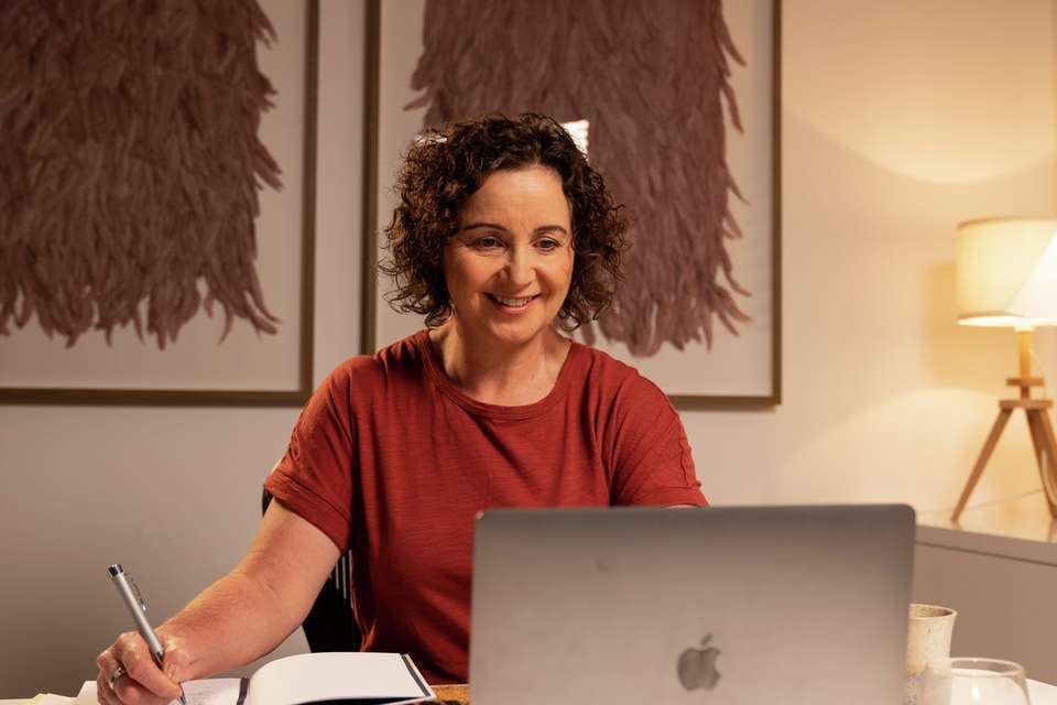 CQU student studying at home using her laptop computer with notepad next to her.