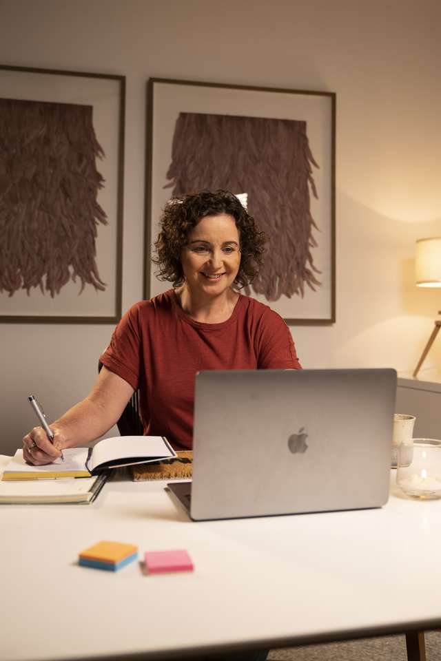 CQU student studying at home using her laptop computer with notepad next to her.