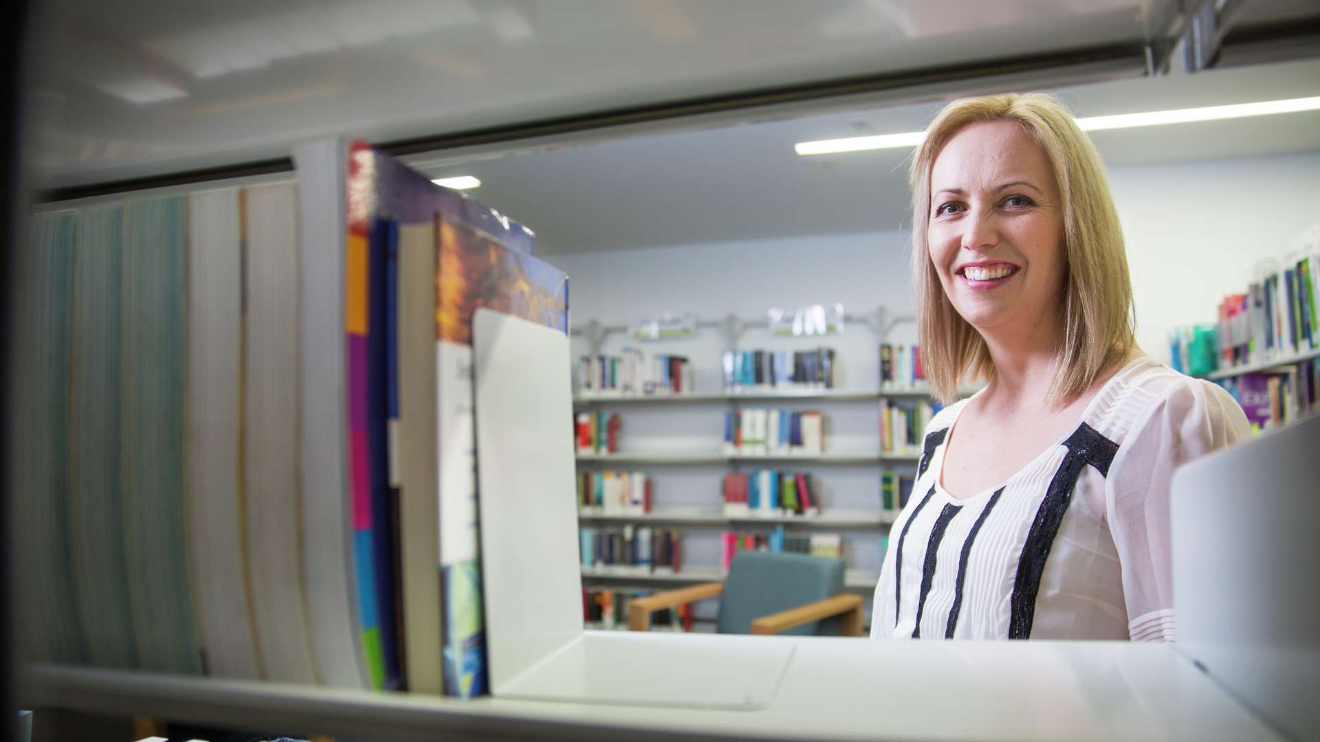 A CQU female student standing in front of a library bookshelf.