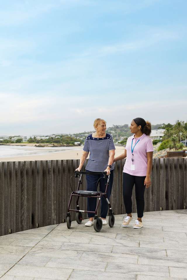 A CQU Community Services student takes a stroll along the esplanade at the beach with an elderly patient who requires assistance with walking