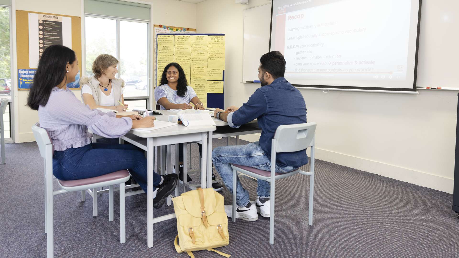 Three students and a teacher sitting around desks doing course work with material projected on a board near them