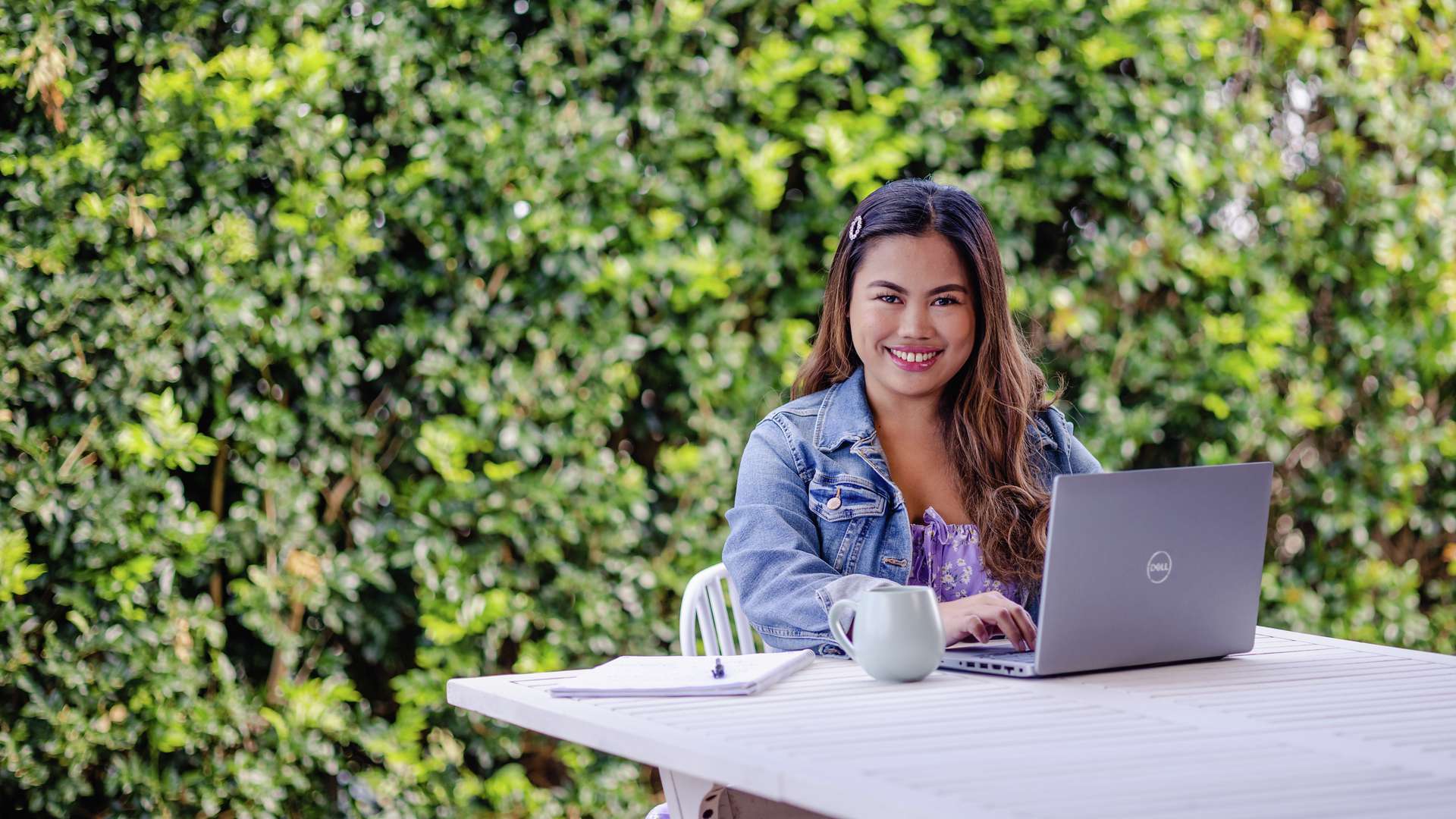 An online student studying at table in garden with laptop
