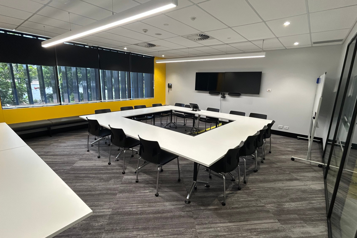 A large U‑shaped conference room with multiple tables, chairs, large windows, and wall‑mounted screens