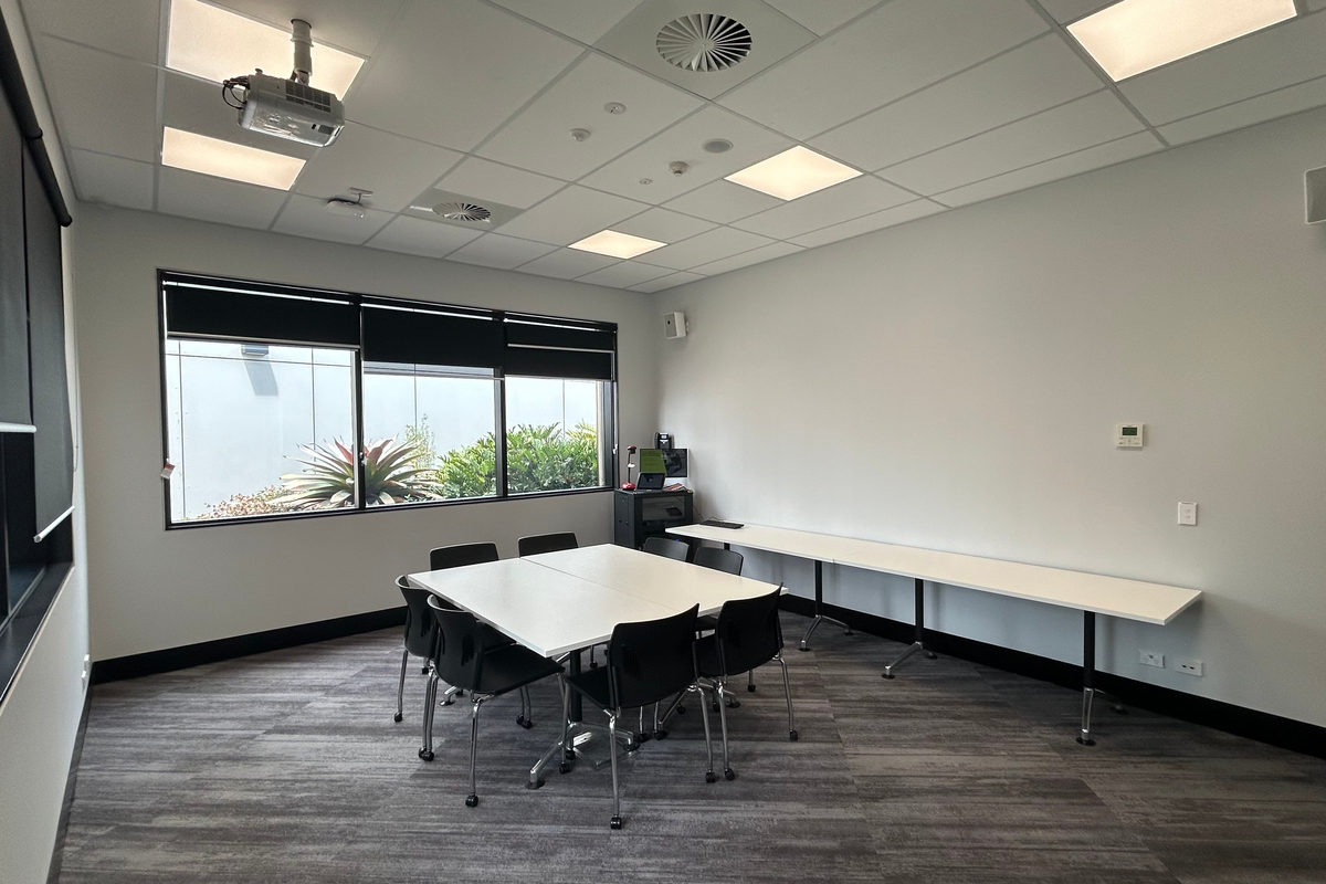 A small meeting room with a central table, chairs, and large windows