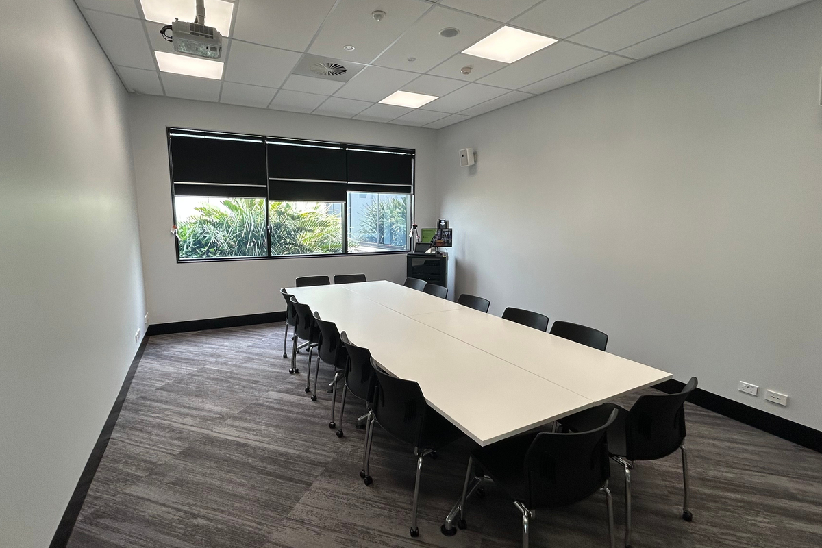 A meeting room with a long table, chairs, and windows facing a garden area.