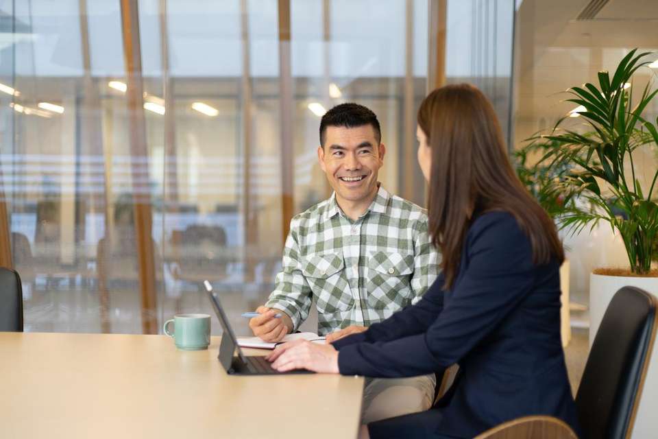 Two students in a corporate setting chatting with a laptop open