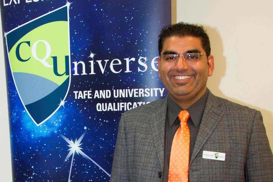 Ritesh smiling with a CQU banner behind him