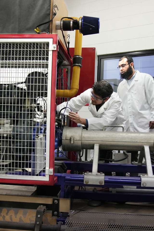 Three engineering students investigating a fuel engine.