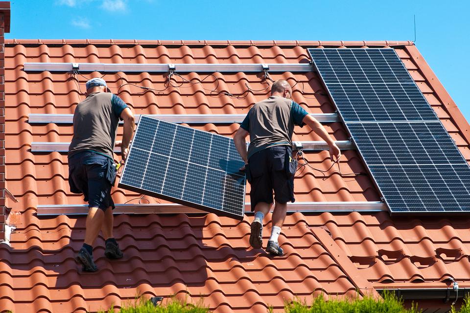 Workers carrying a solar panel on a roof for installation