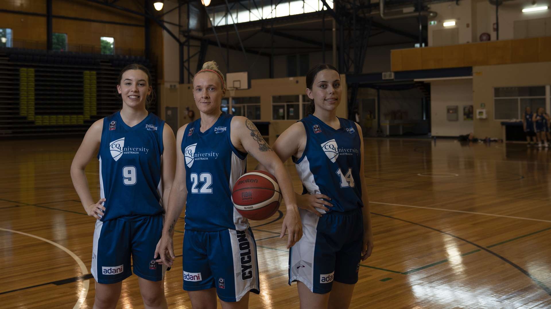 Three Cyclone basketball players posing in the CQU Sports Centre with a basketball