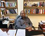 Stanley Liria sitting at their desk with shelves of books behind