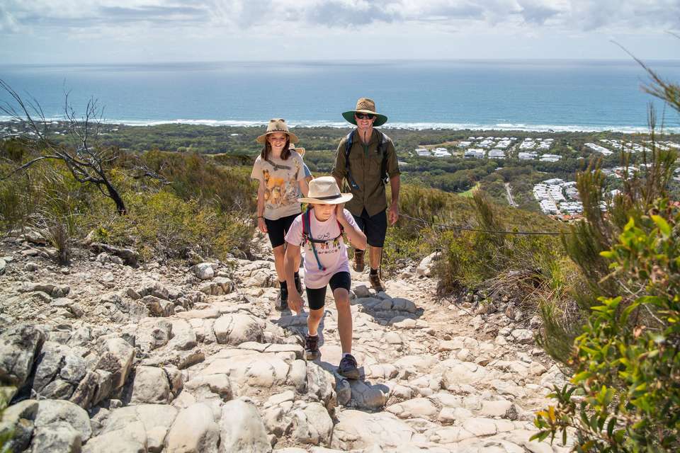 A family of three walk up a hill with the ocean in the background.