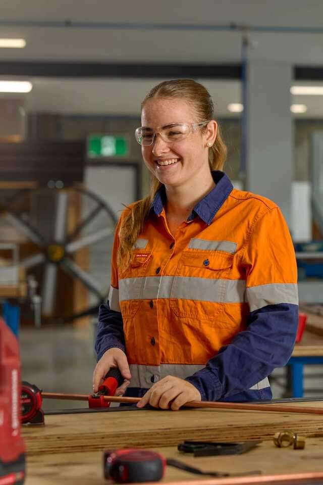 Student wearing a high vis long sleeve shirt and safety glasses cutting a piece of metal pipe in the TAFE Excellence workshop
