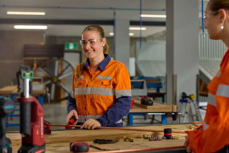 Student wearing a high vis long sleeve shirt and safety glasses cutting a piece of metal pipe in the TAFE Excellence workshop