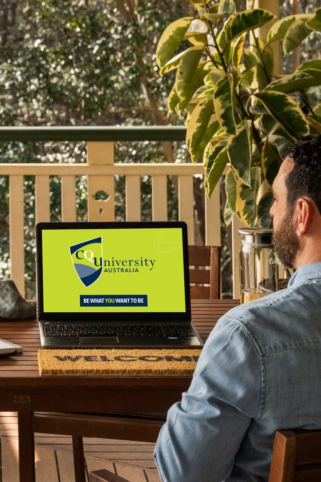 Student sitting on veranda studying online with a laptop showing CQUniversity logo