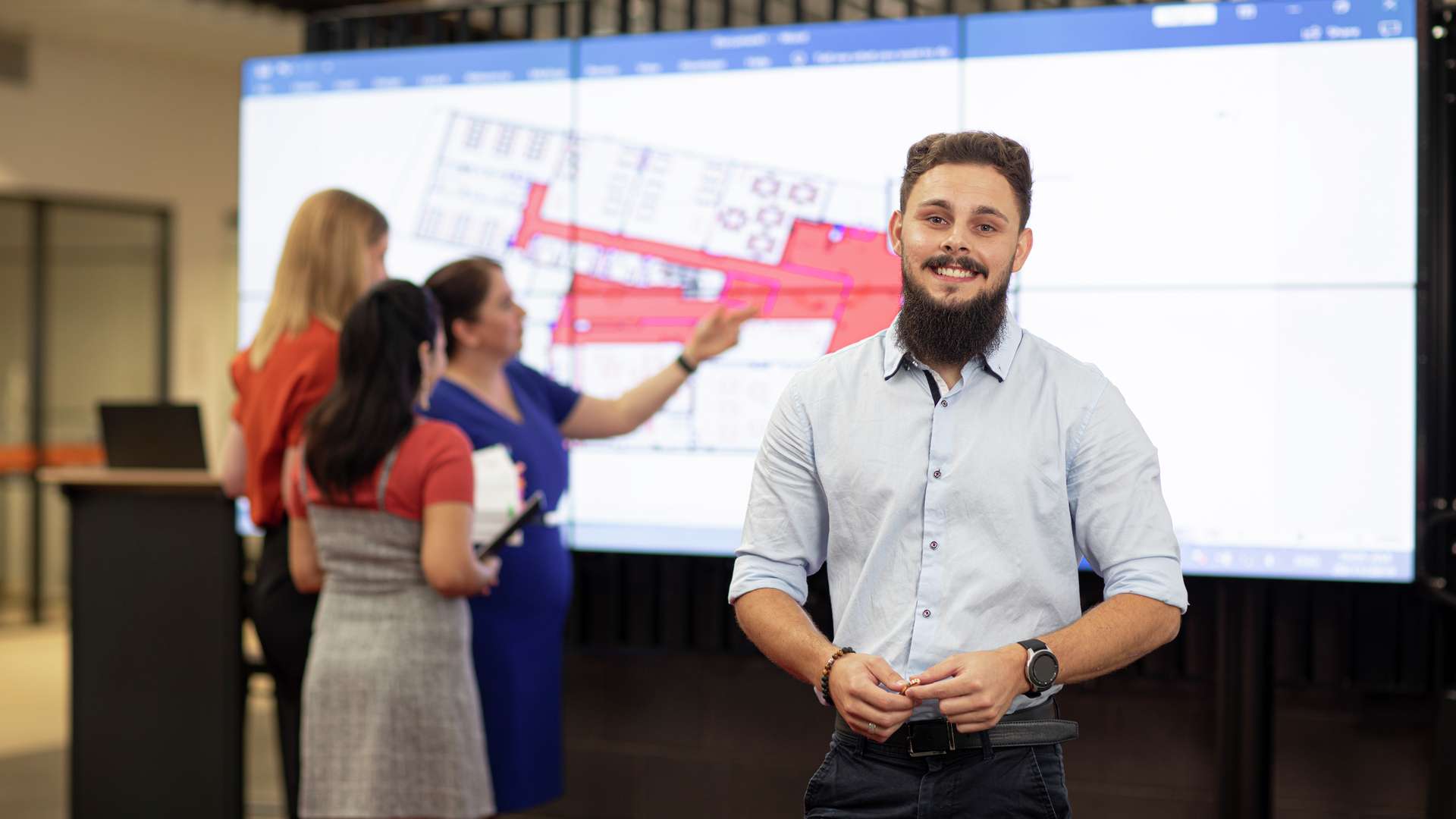 Building Design student standing in front of PowerPoint Presentation that is being inspected by other students behind him