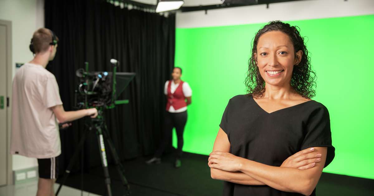 Digital Media students smiling as her fellow students stand in the background with a camera
