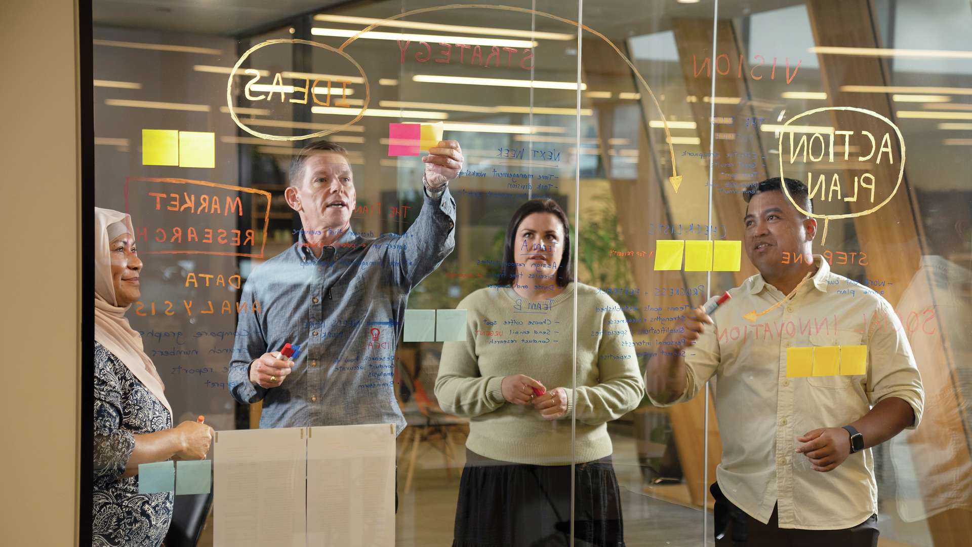 Students put together a plan for their team project by drawing a diagram. on a glass wall.
