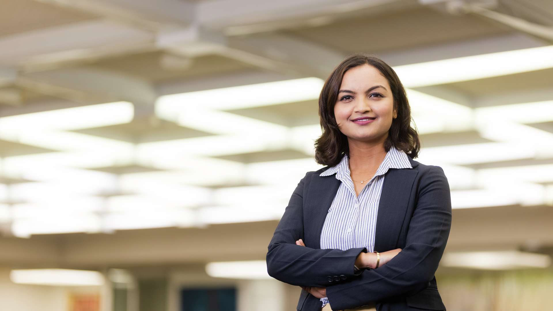 An MBA student stands in an office with crossed arms smiling confidently at the camera.