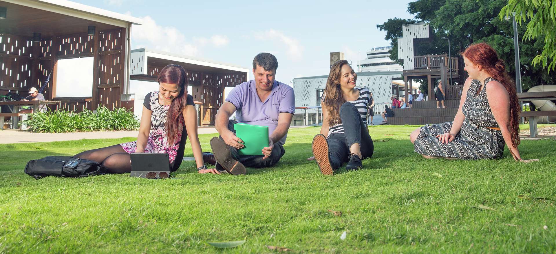 CQU students sitting, chatting and studying on the grass under a blue sky on campus