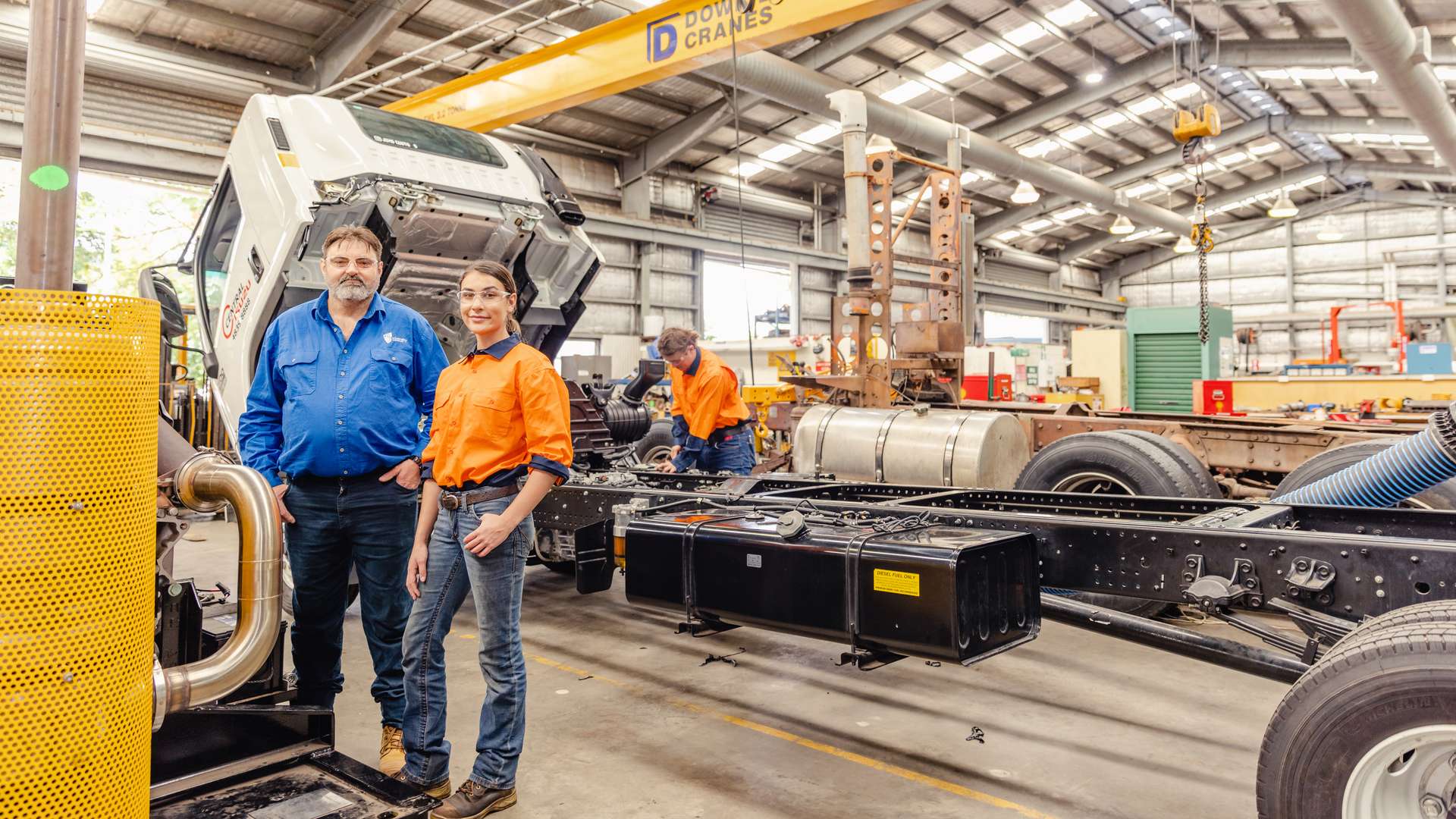 Mechanical engineering students smiling in the foreground of a mechanical garage.