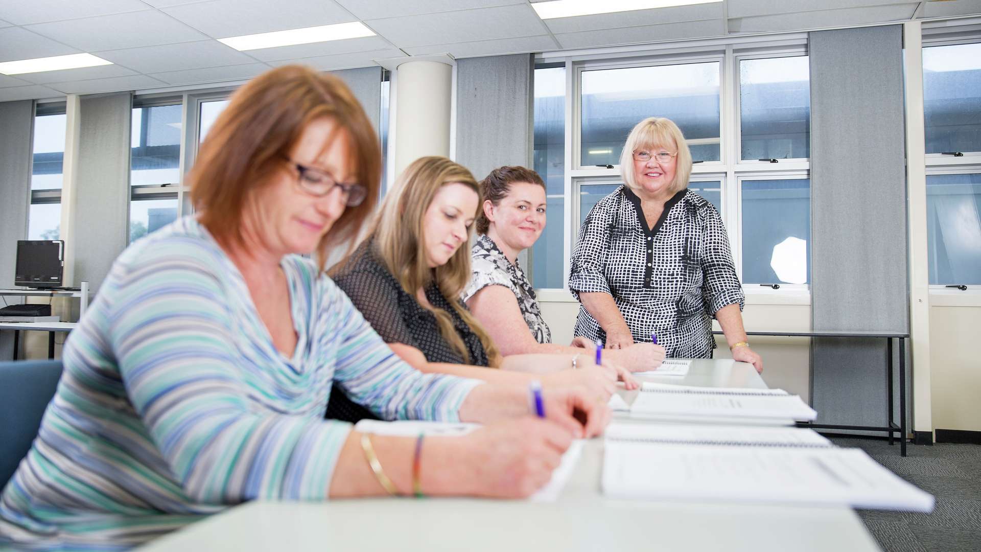 Students writing in workbooks in a tutorial room with teacher assisting