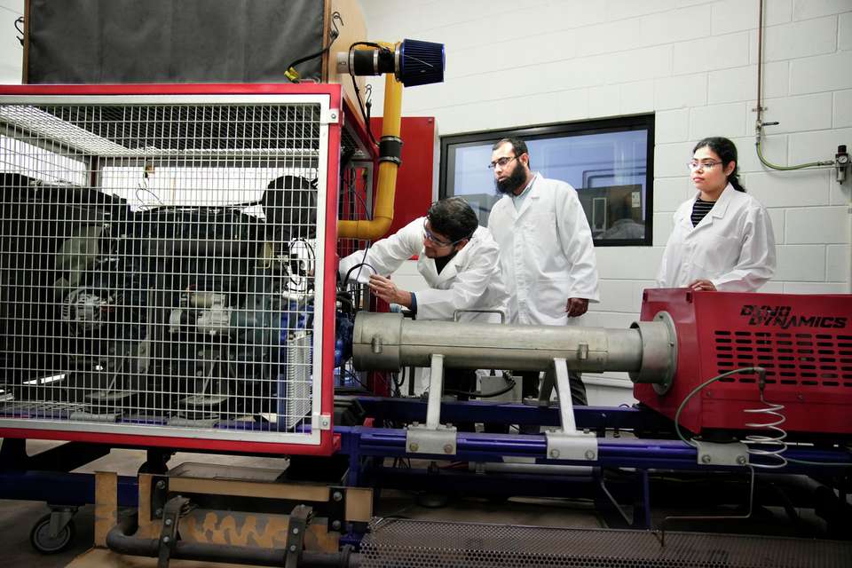 Three engineering students investigating a fuel engine.