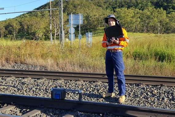 A researcher standing on railway tracks holding a laptop