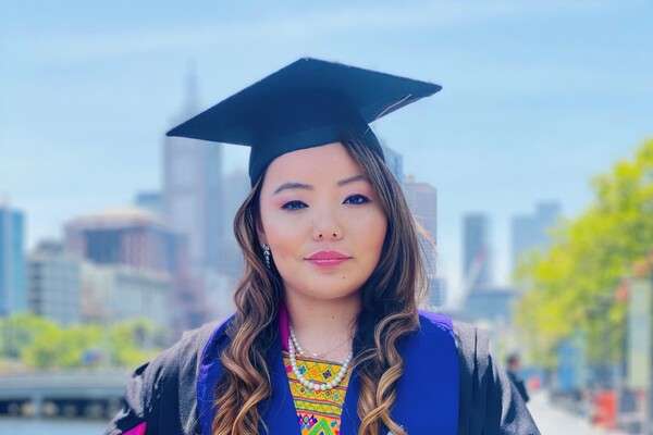 Masters Student, Tshering Choki from Bhutan, wearing the CQU graduation Cap and Gown smiling with the Melbourne skyline behind her
