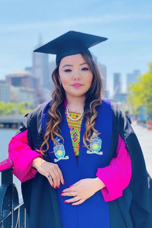 Masters Student, Tshering Choki from Bhutan, wearing the CQU graduation Cap and Gown smiling with the Melbourne skyline behind her