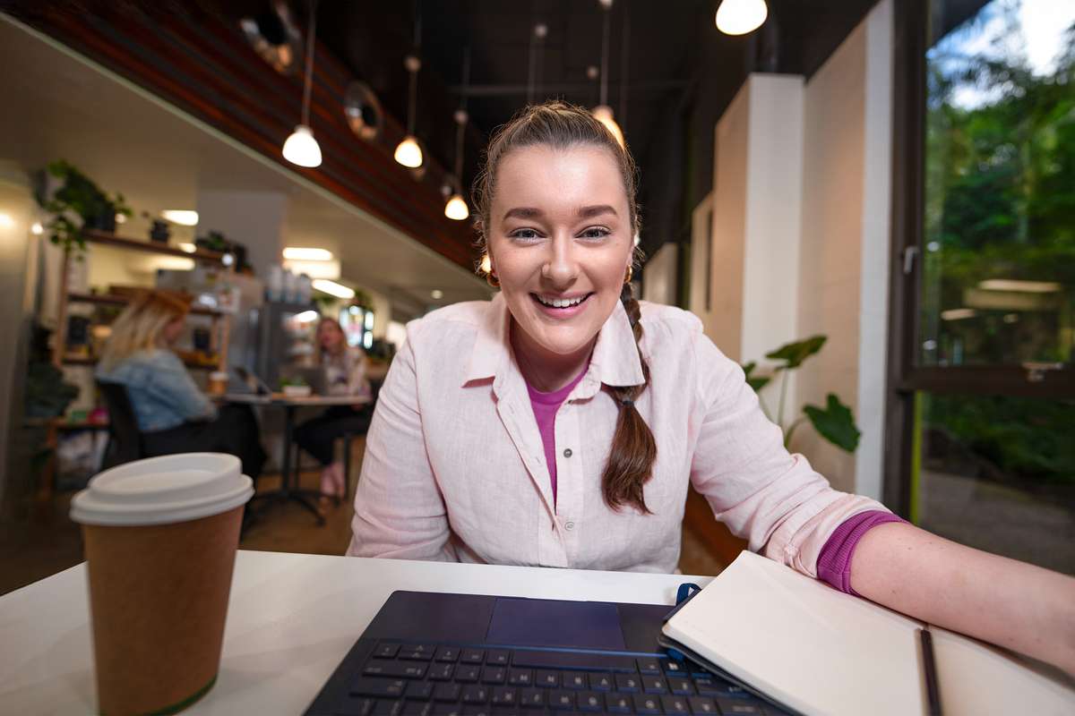 A CQU student smiles while looking at the computer, the point of view is from the computer screen.